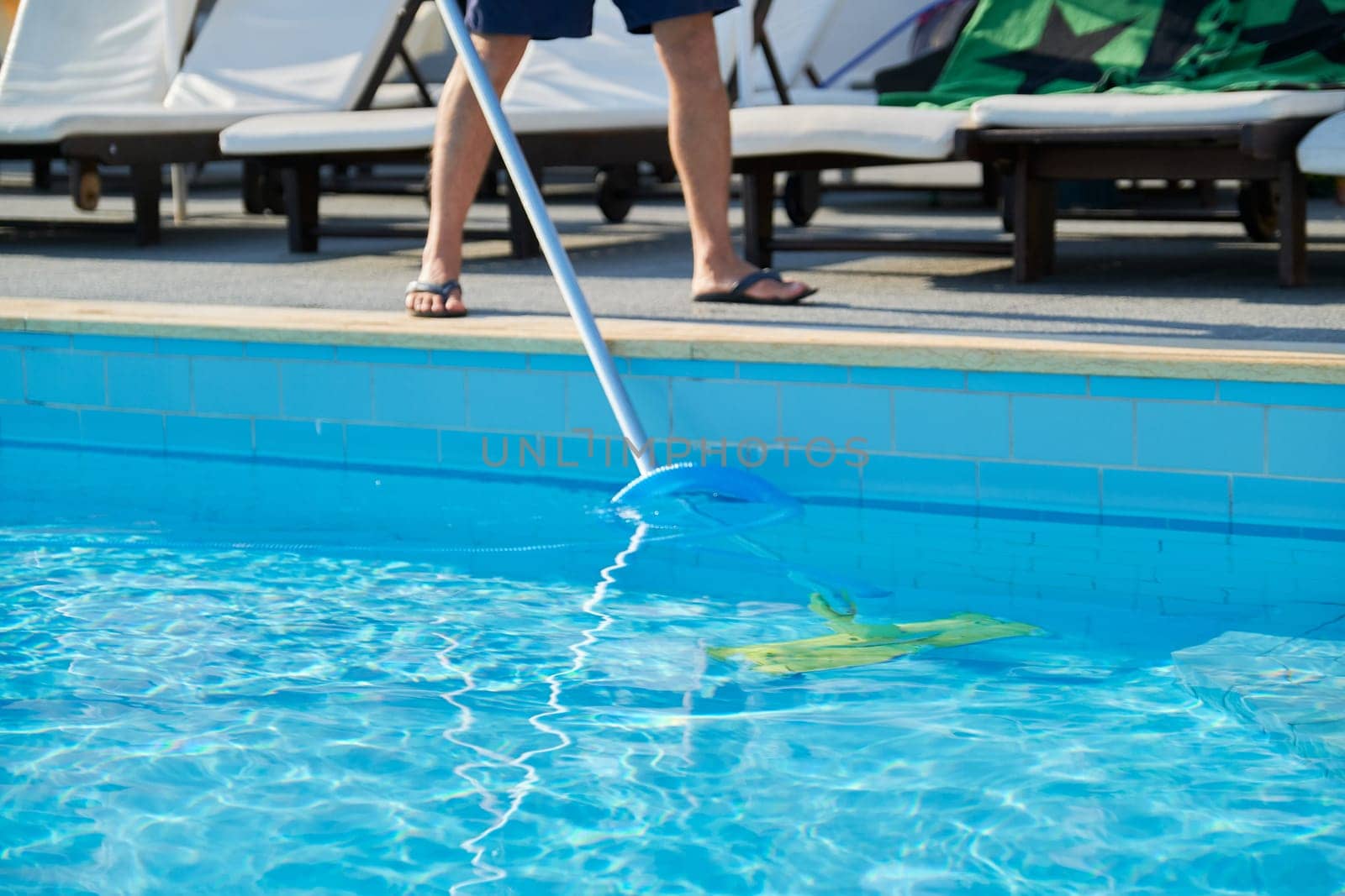 Male cleaning outdoor swimming pool with underwater vacuum tube by VH-studio