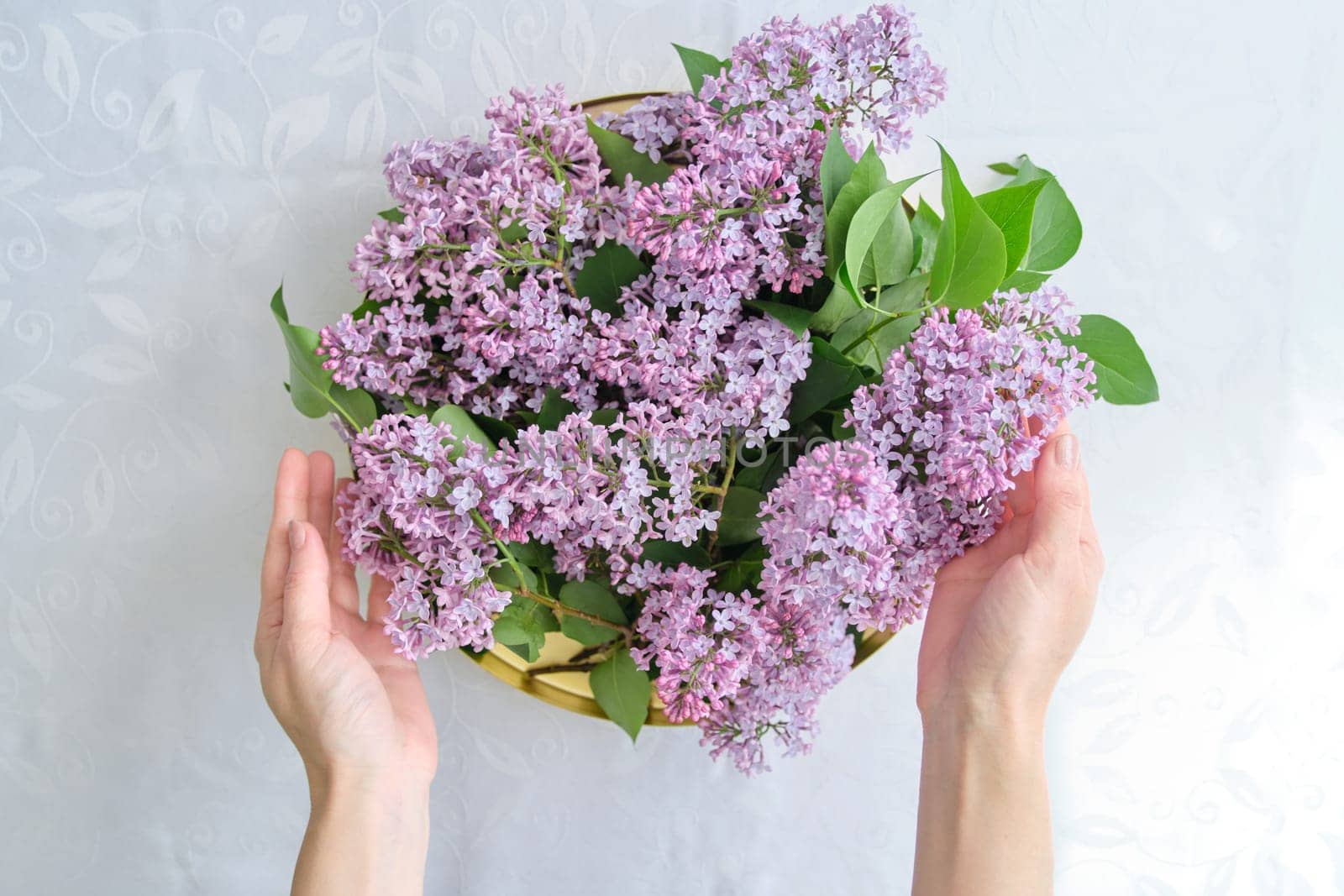 Woman florist with lilac floral decoration. Light background, female holding golden tray with flowers in her hands for interior decoration