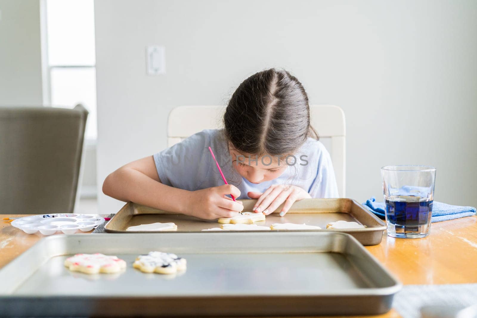 A heartwarming scene of a little girl carefully writing 'Sorry' on sugar cookies with food coloring, the cookies beautifully flooded with white royal icing.