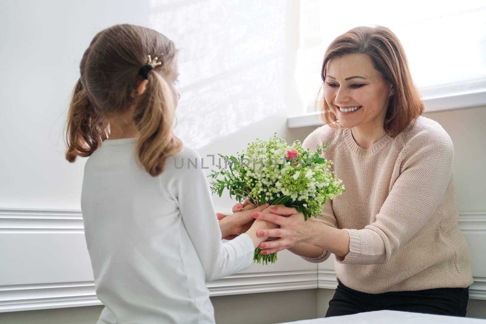 Little girl giving a bouquet to her mother. Daughter congratulating mom on beautiful spring flowers on mother's day