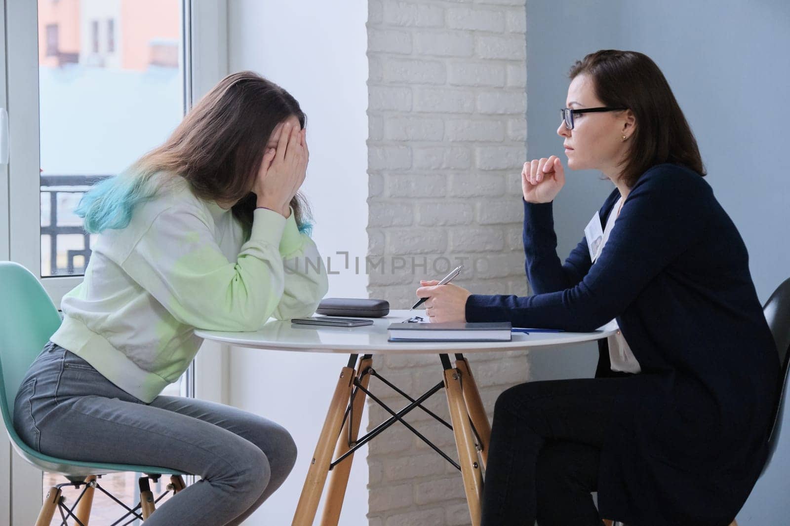 Teen girl covered face with hands at meeting with psychologist. Problems of adolescent children, help of therapist, mental health of young people