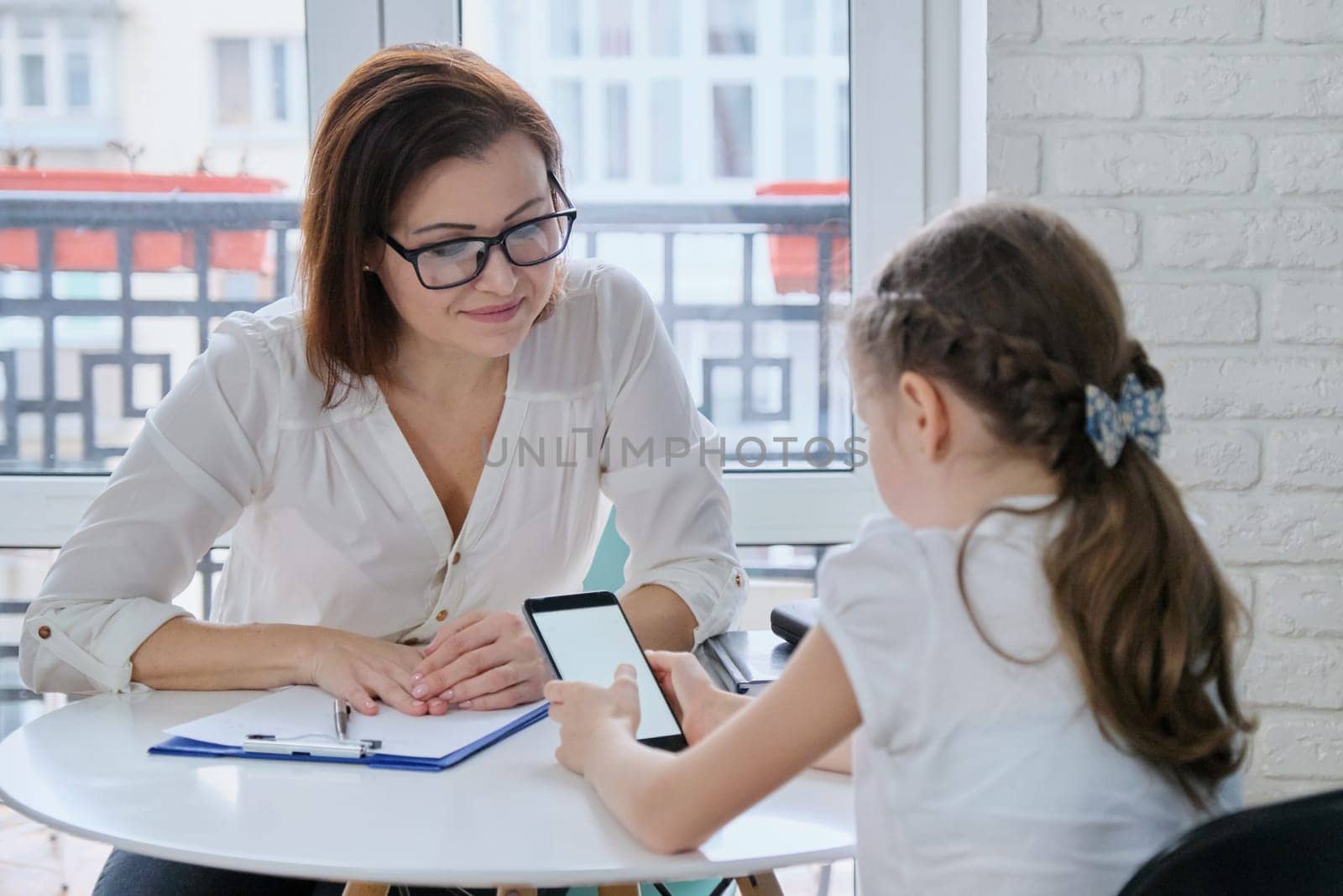 Girl at meeting with psychologist showing his social page on smartphone, talking psychiatrist and child, mental health of children