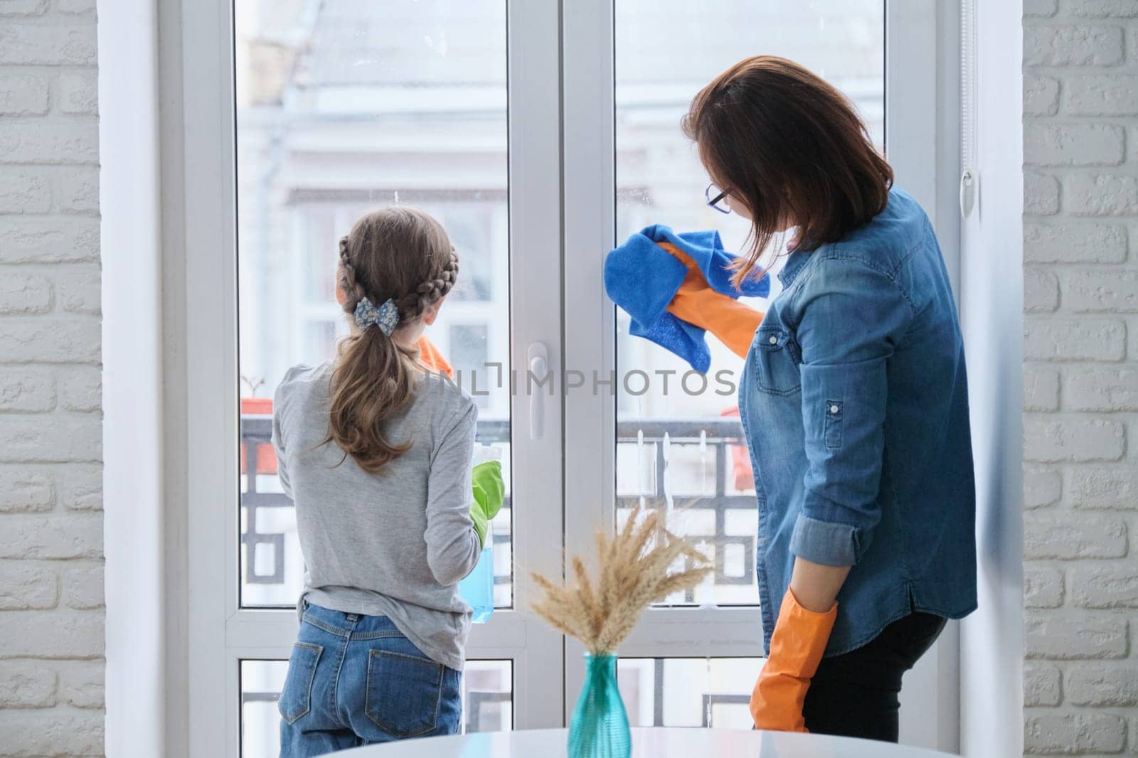 Mother and daughter child in gloves with detergent rag cleaning windows together by VH-studio