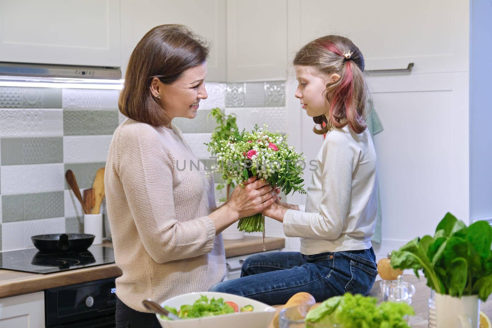 Mothers day, daughter child gives mother bouquet of spring flowers, background interior home kitchen