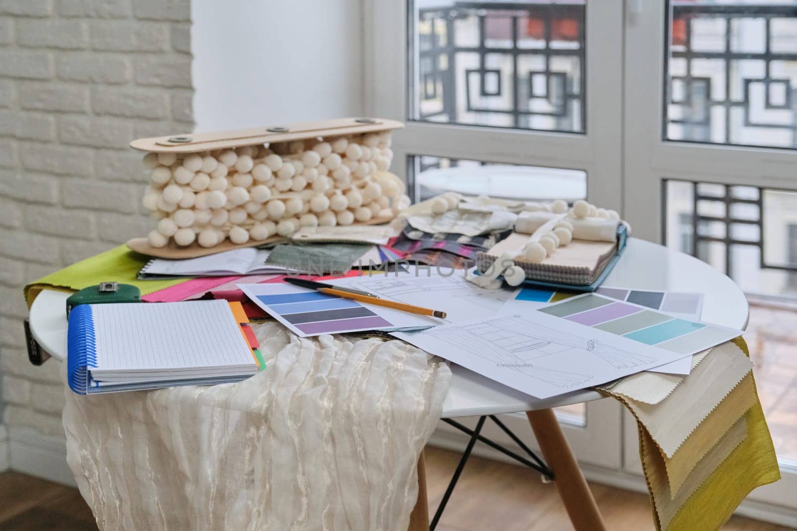 Workplace of textile designer, interior decorator. On the desk palettes with fabrics, drawings with models of curtains, accessories, notebook with notes