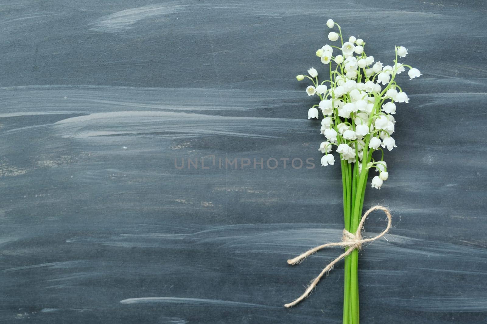 Spring flowers lily of the valley on gray vintage painted background, flat lay with small bouquet, place for text, copy space, view from above