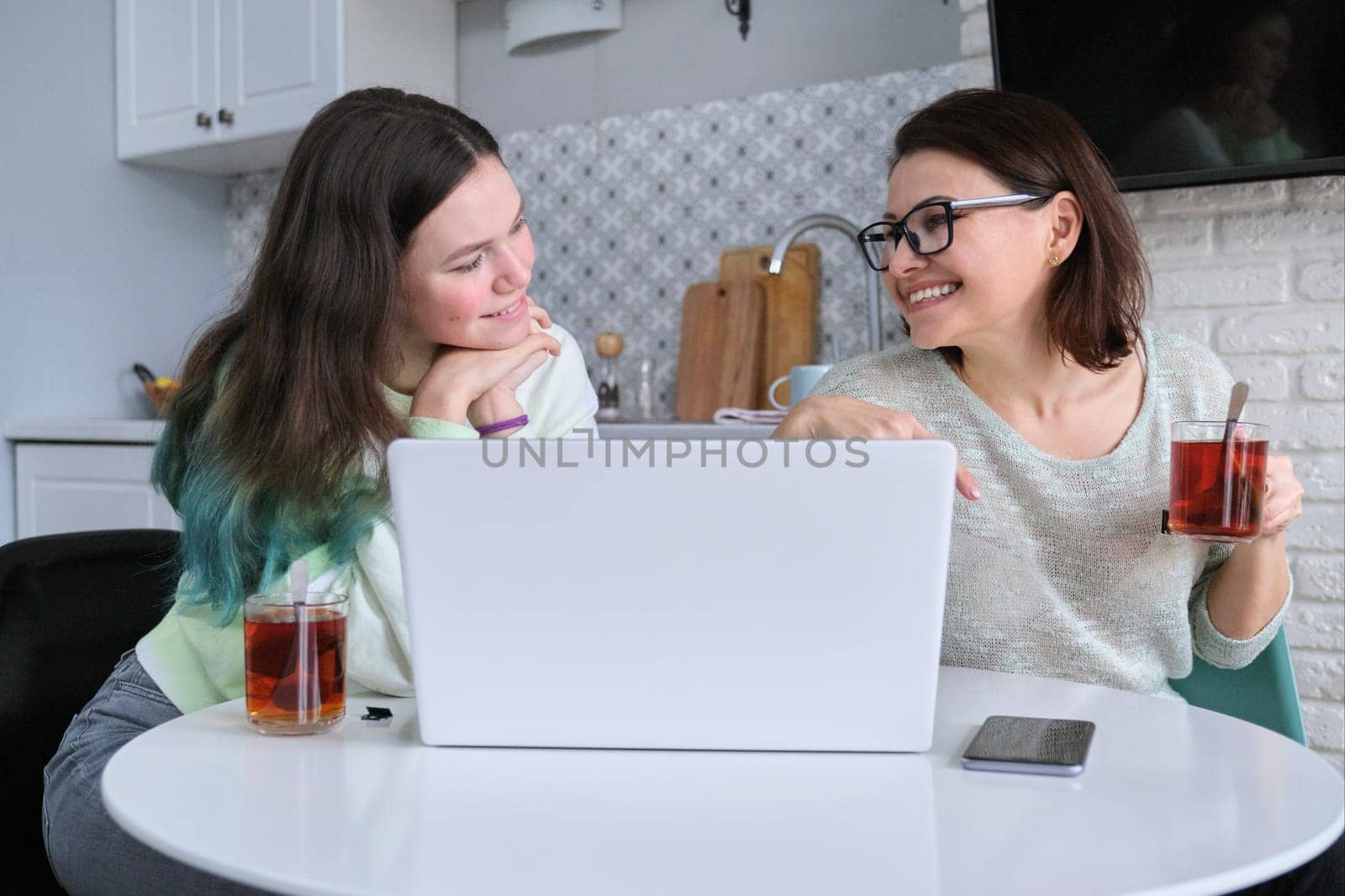 Parent and teenager sitting at home in kitchen and looking at laptop screen by VH-studio