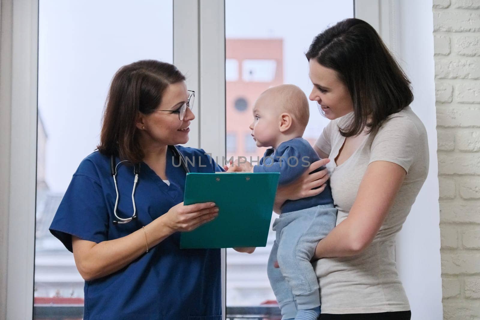 Doctor pediatrician talking with young mother holding her baby in her arms by VH-studio
