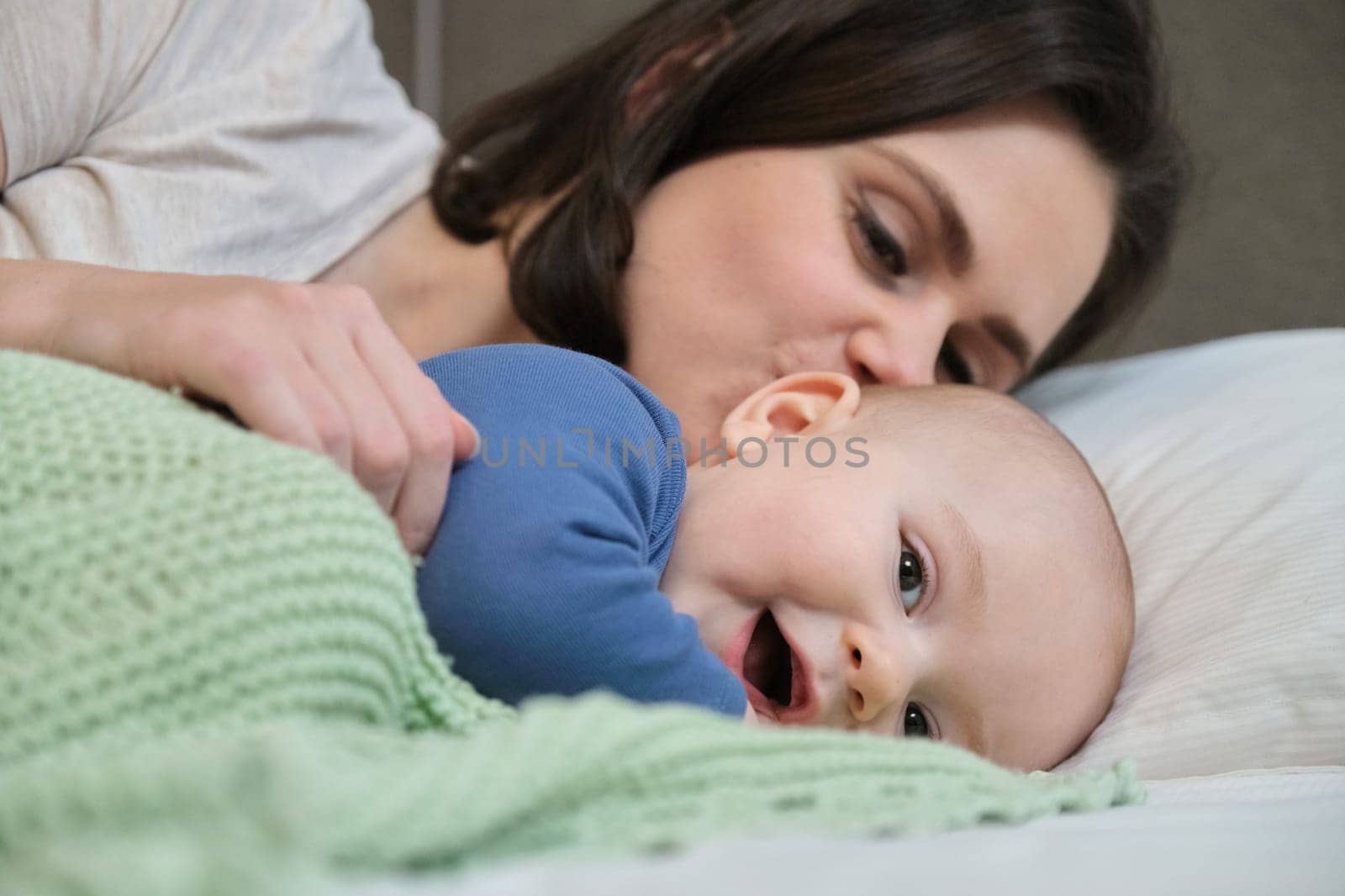 Portrait of beautiful young mother and her baby 7 month old son, parent and baby lying in bed together