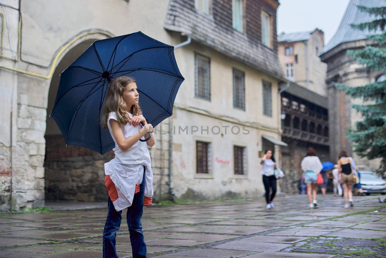 Little girl child in the rain with an umbrella, tourist old city background, copy space