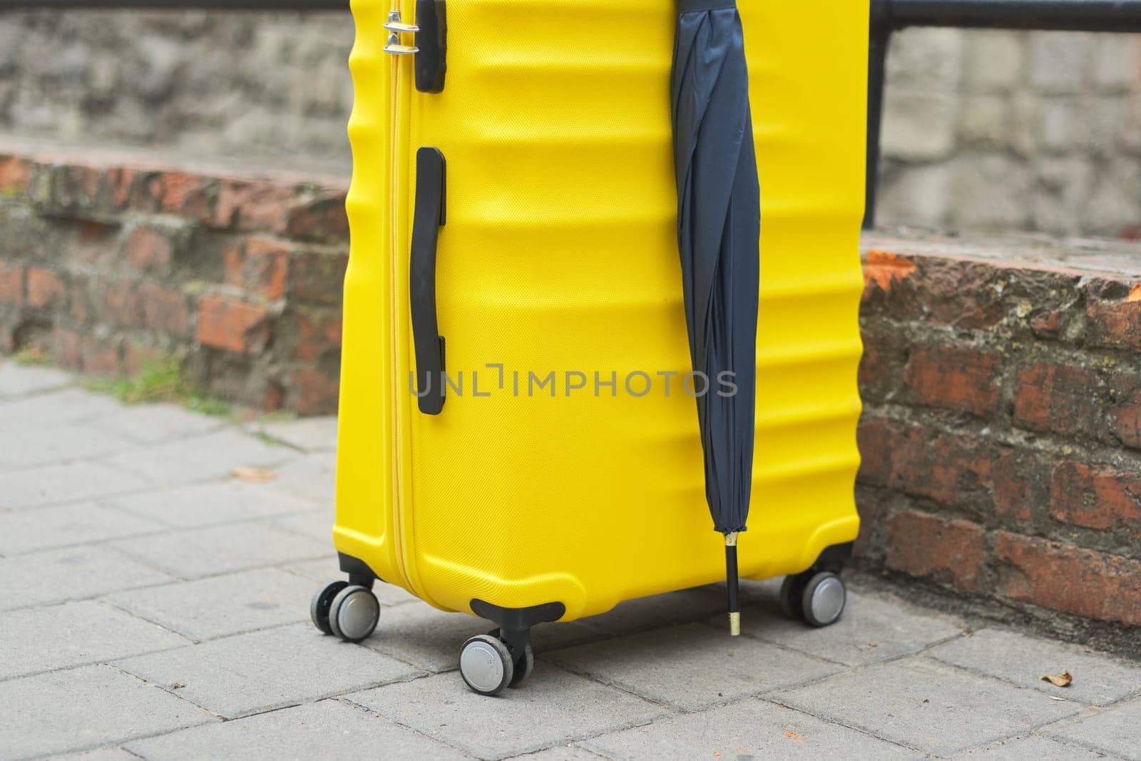 Travel tourism concept, close up of yellow plastic suitcase, umbrella, on tourist city street