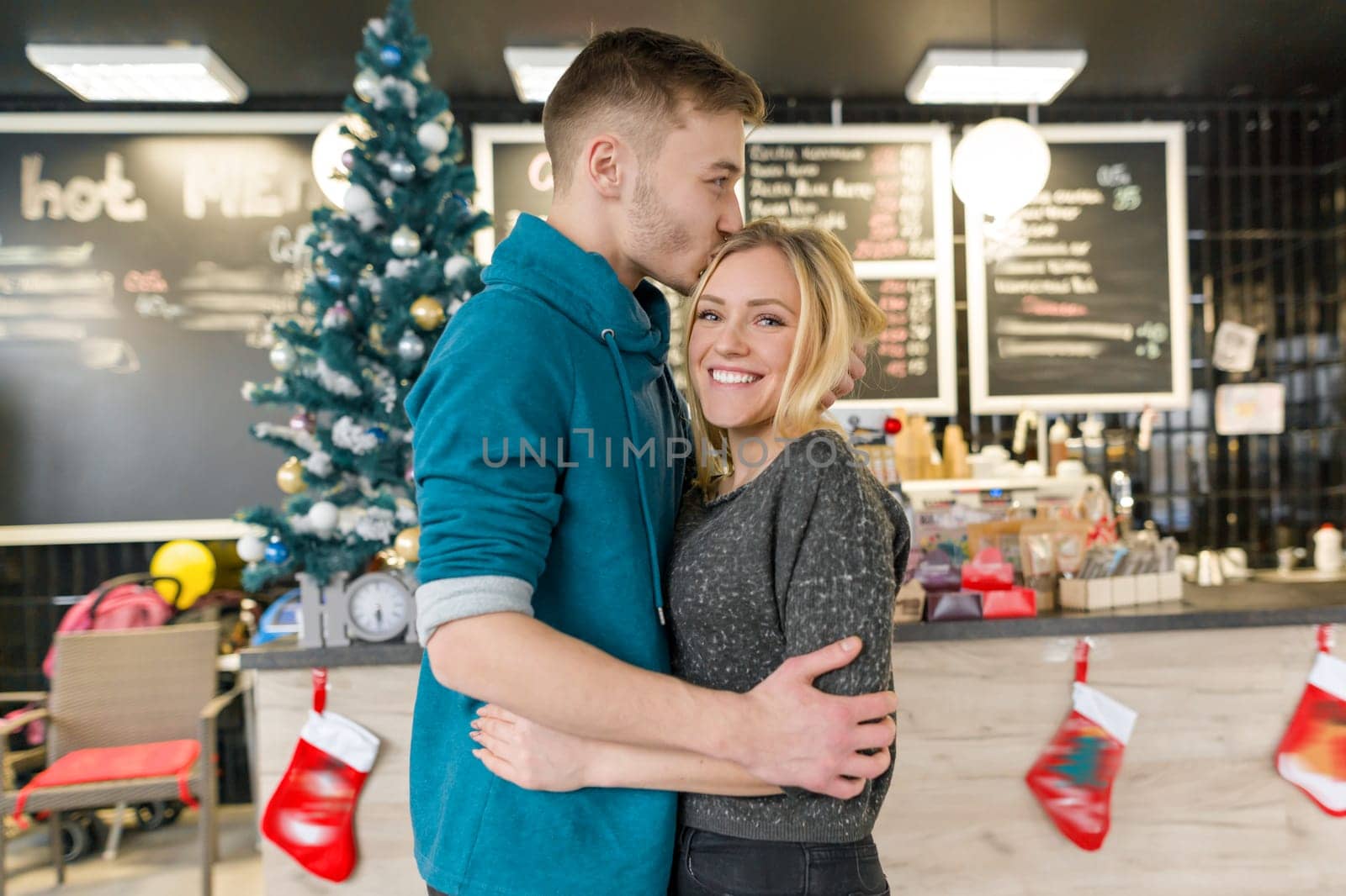 Kissing young couple near Christmas tree in cafe.