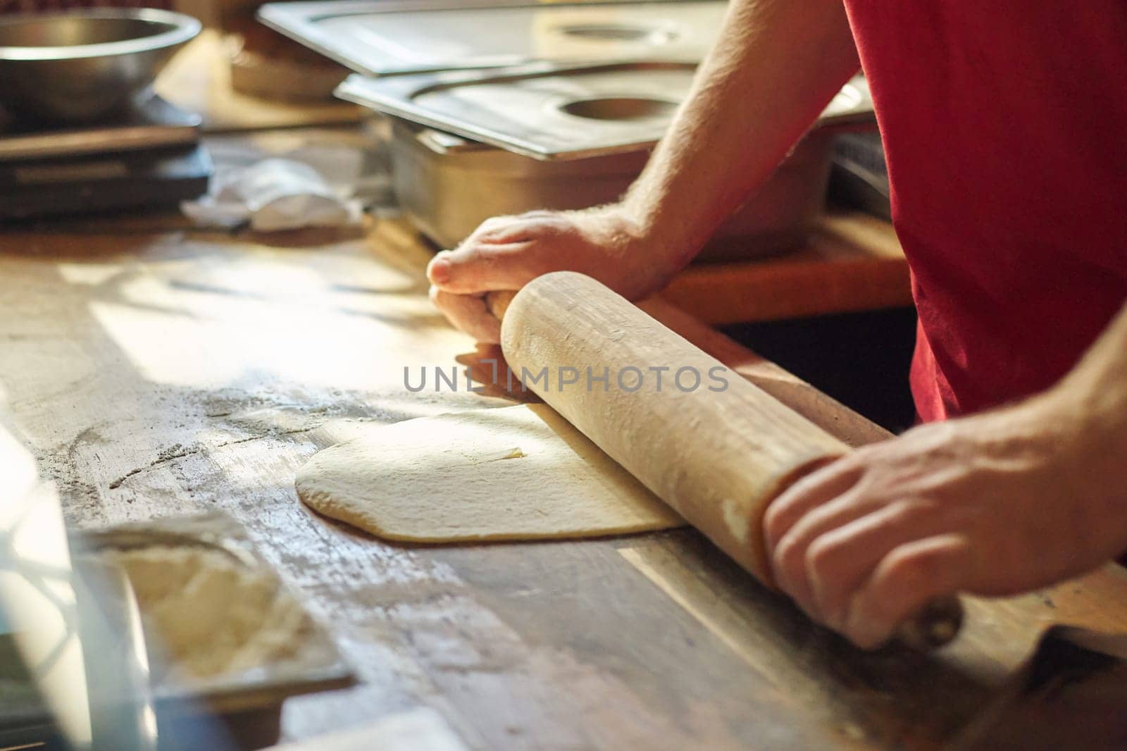 Close up of male baker hands with flour cook roll out the dough with rolling pin on wooden table in kitchen