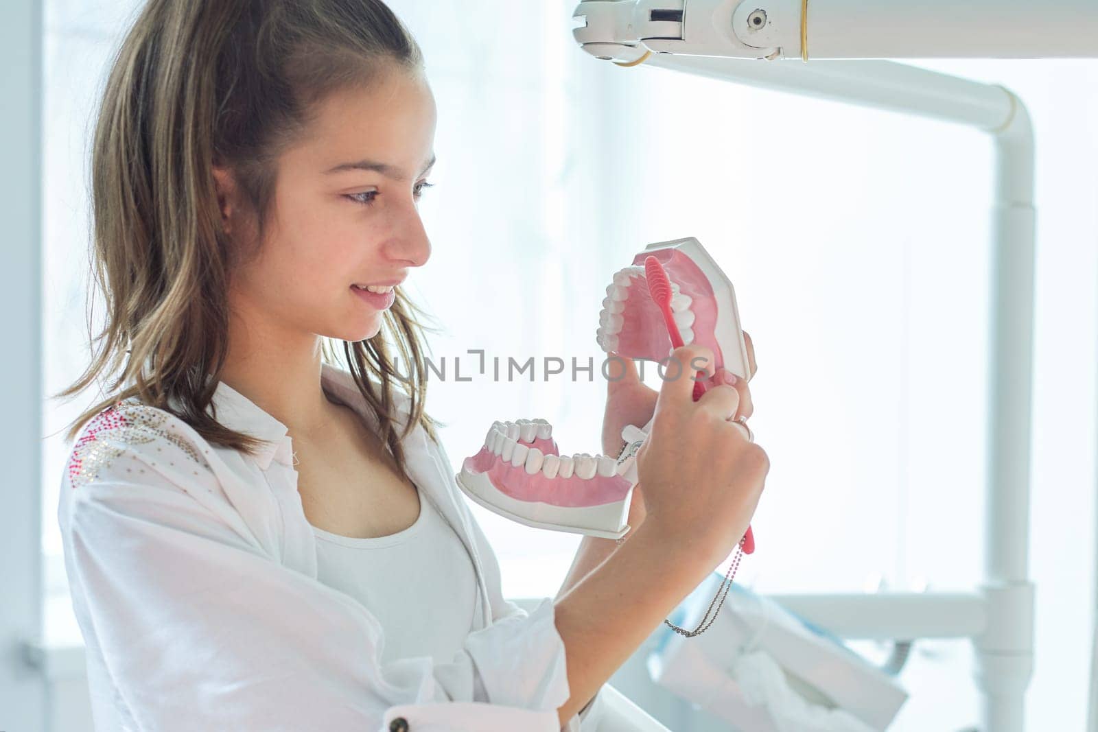 Smiling teenager girl in dental office holding jaw model with teeth in her hands