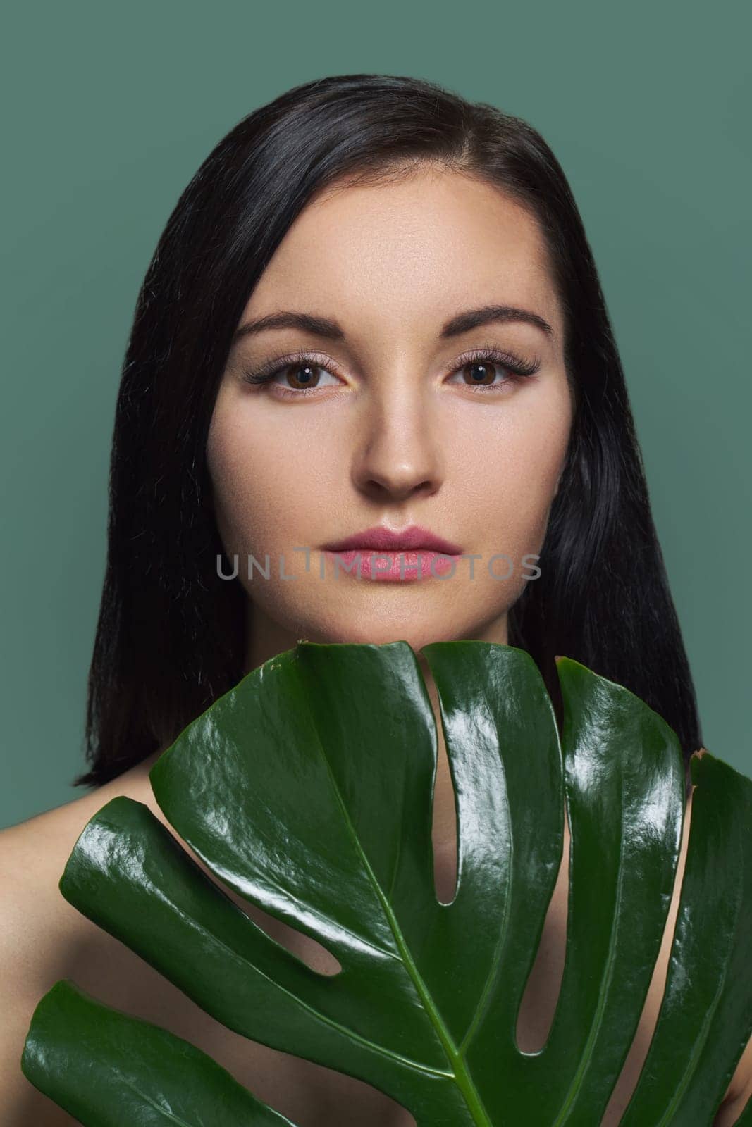 Closeup portrait of young beautiful woman with green leaf, female with natural beauty, no make-up, with extended eyelashes, green background