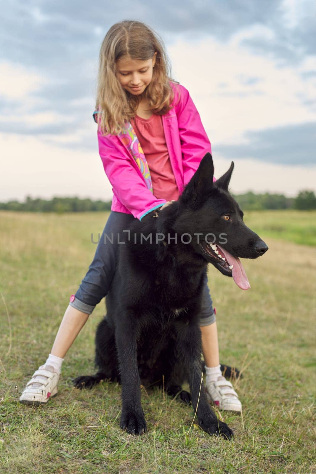 Girl hugging big black dog shepherd, child and pet walking in nature.