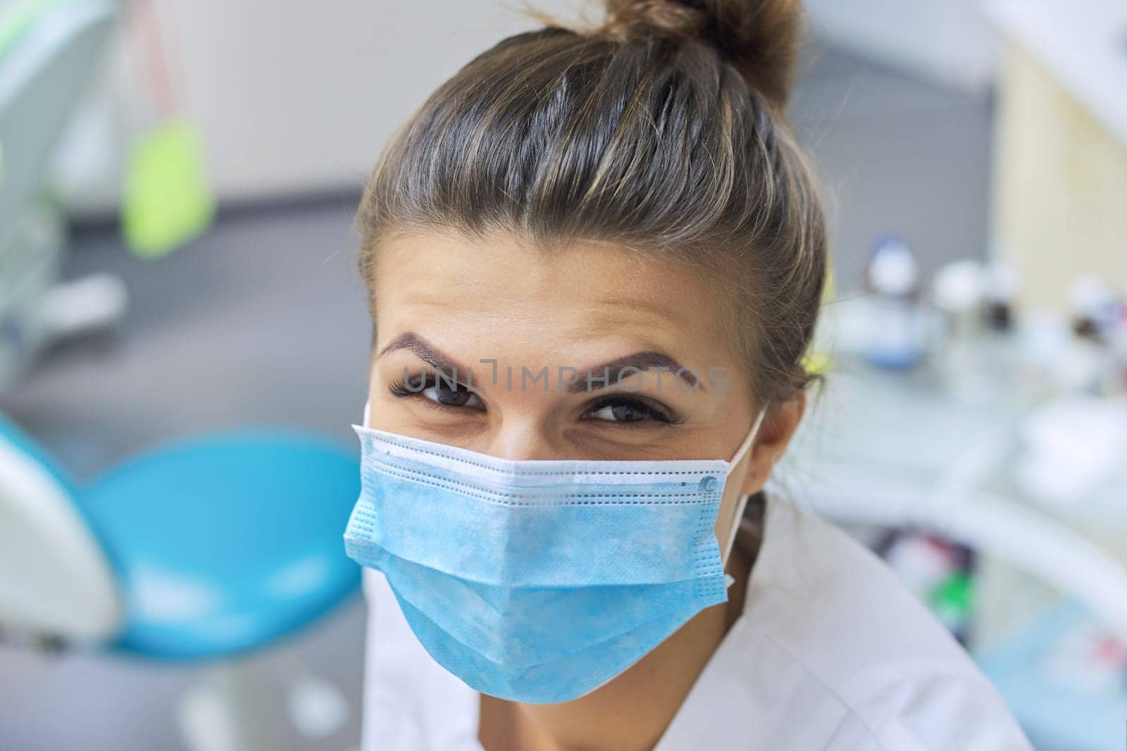 Closeup portrait of smiling female dentist doctor in protective medical mask at workplace dental clinic office, positive face