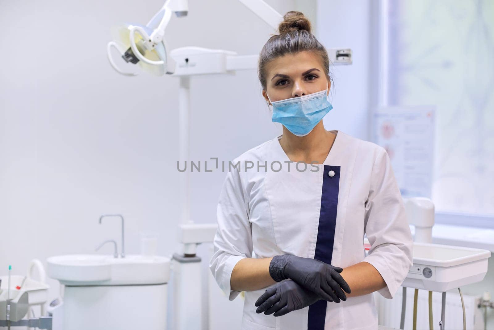 Portrait of confident female dentist doctor in white coat with mask near dental chair in dental clinic office