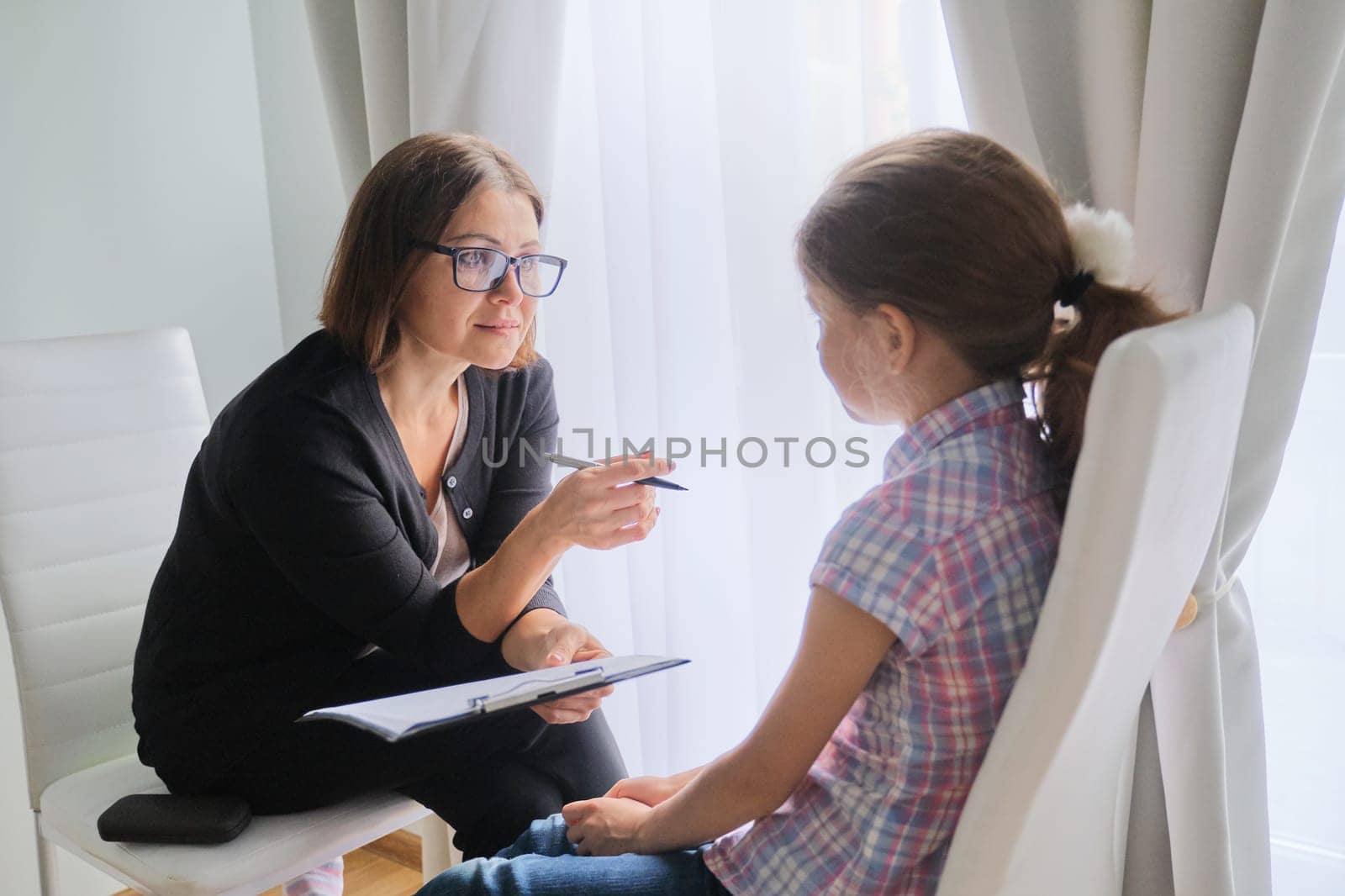 Talking girl and woman psychotherapist in office near window. Child psychology, mental health