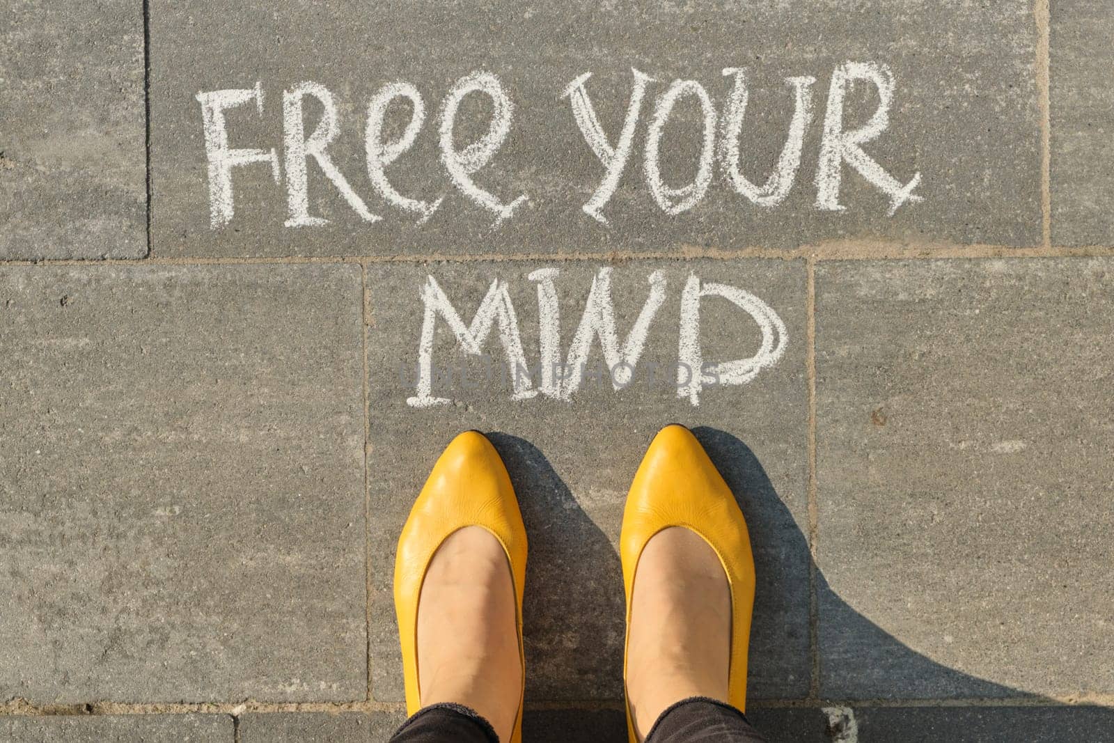 Free your mind text on gray sidewalk with woman legs, top view.