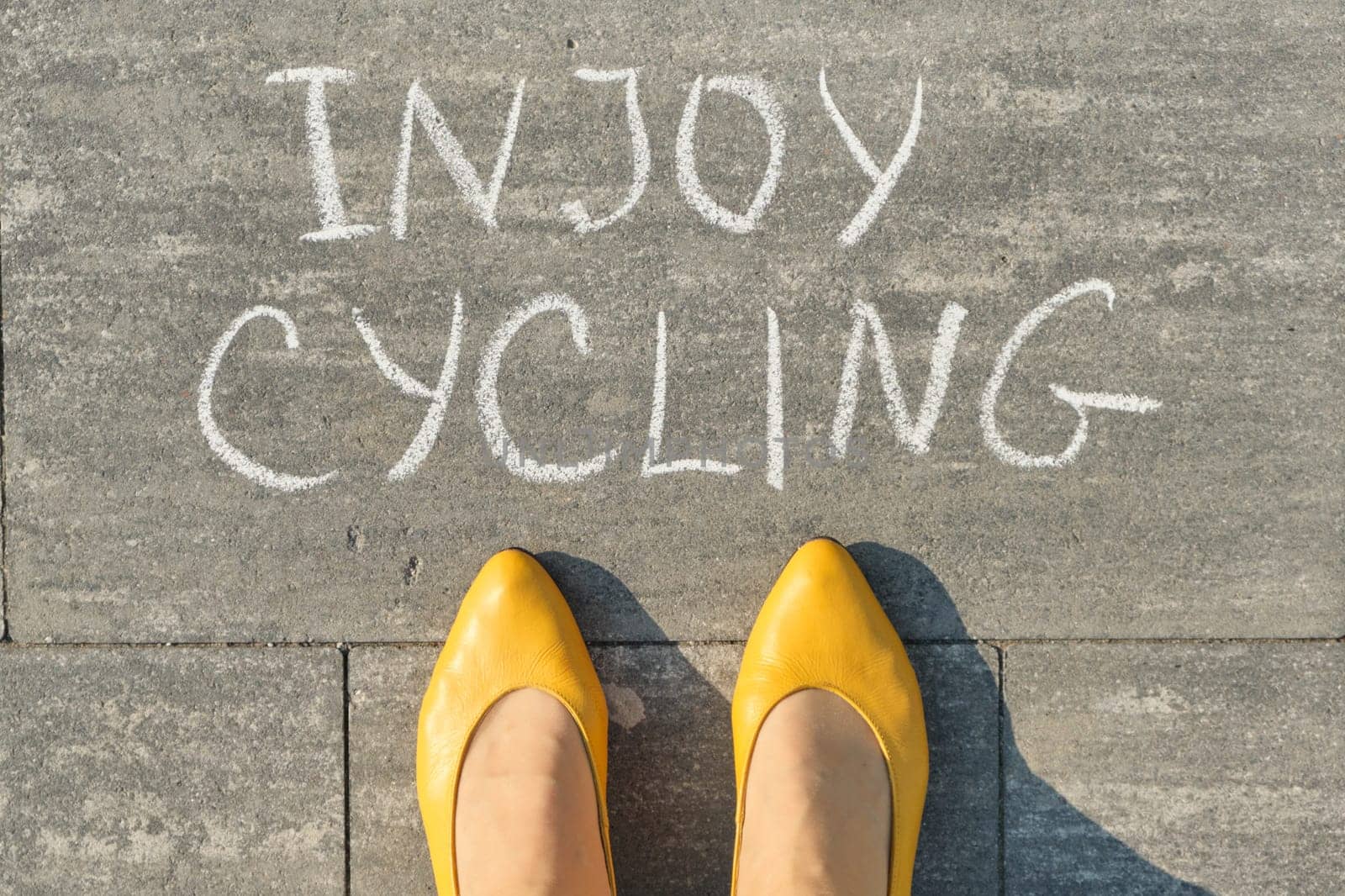 Enjoy cycling, text on gray sidewalk with woman legs, top view by VH-studio