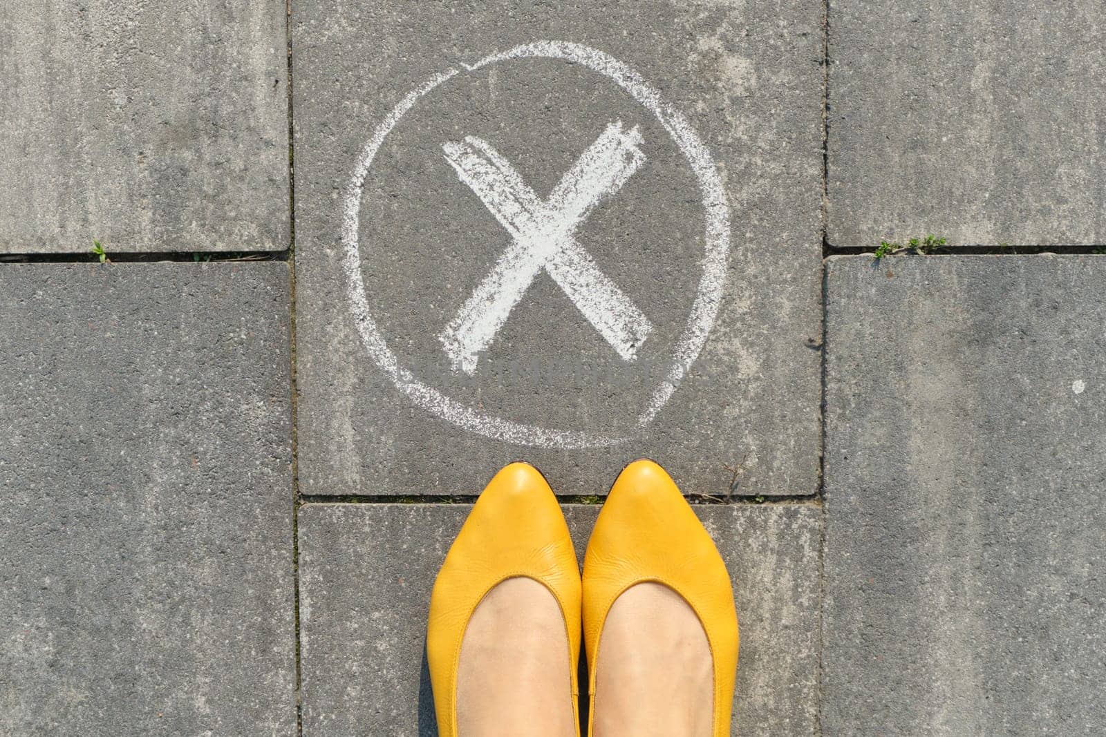 Checkmark no sign on gray sidewalk with woman legs, top view.