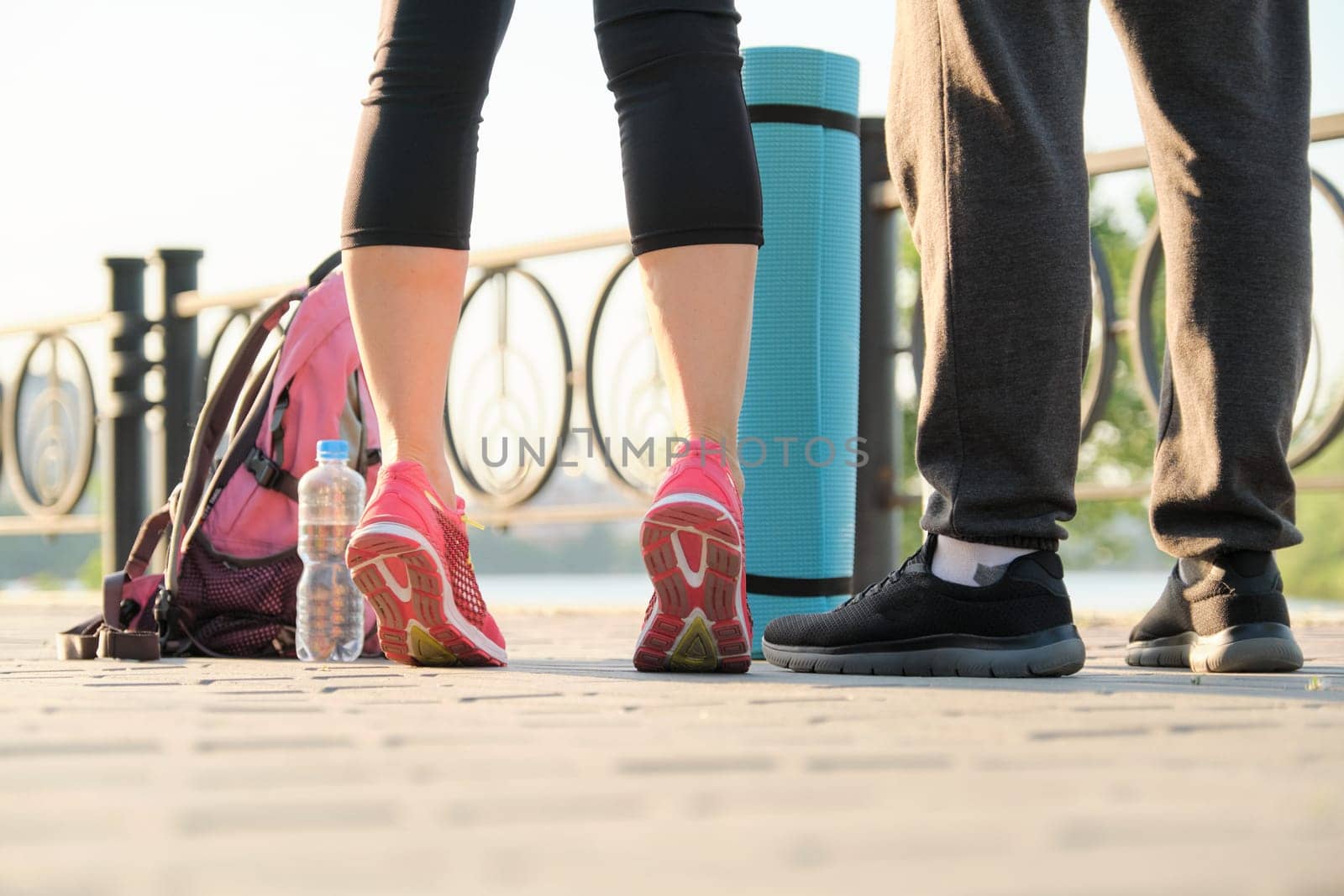 Close-up of couple legs in sneakers with water bottle of exercise mat by VH-studio