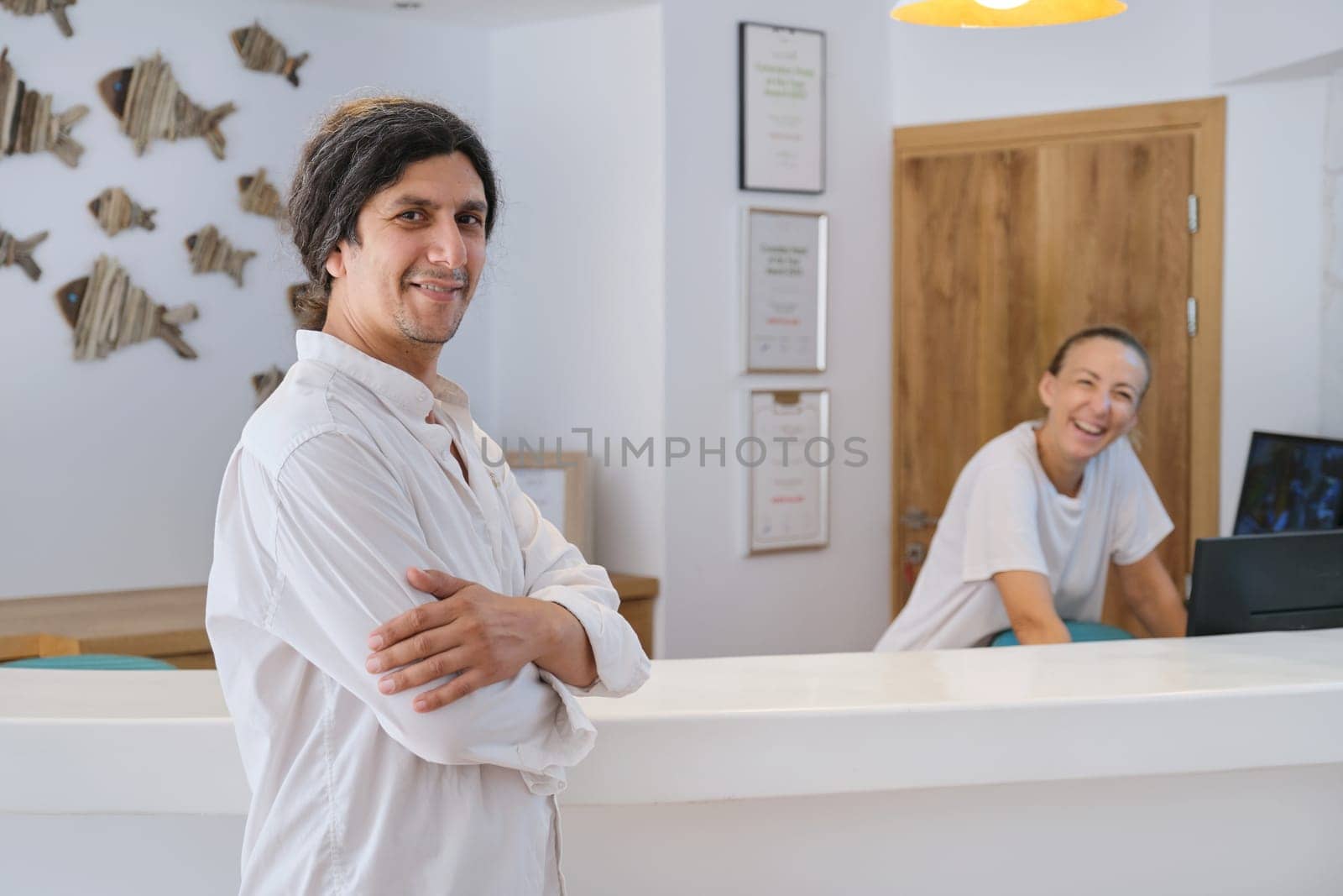 Man hotel manager standing near front desk, woman working at reception.