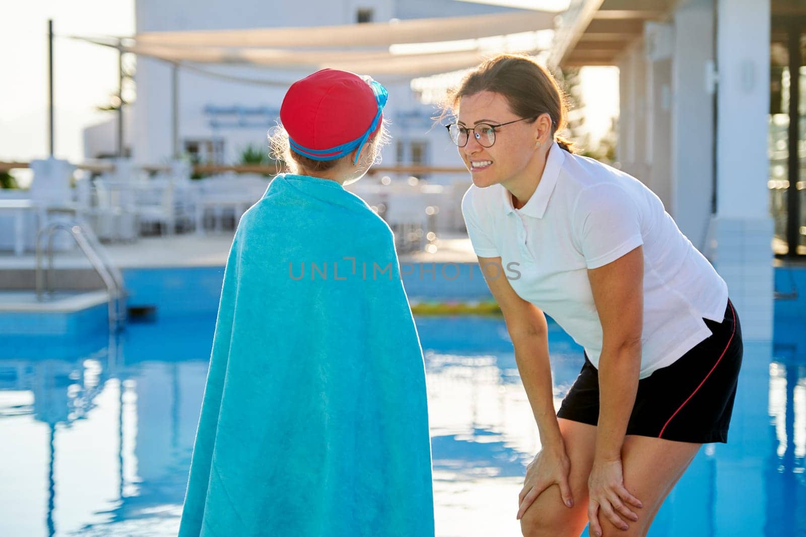 Active healthy lifestyle, mother and daughter child in sport hat goggles for swimming with towel near the outdoor pool