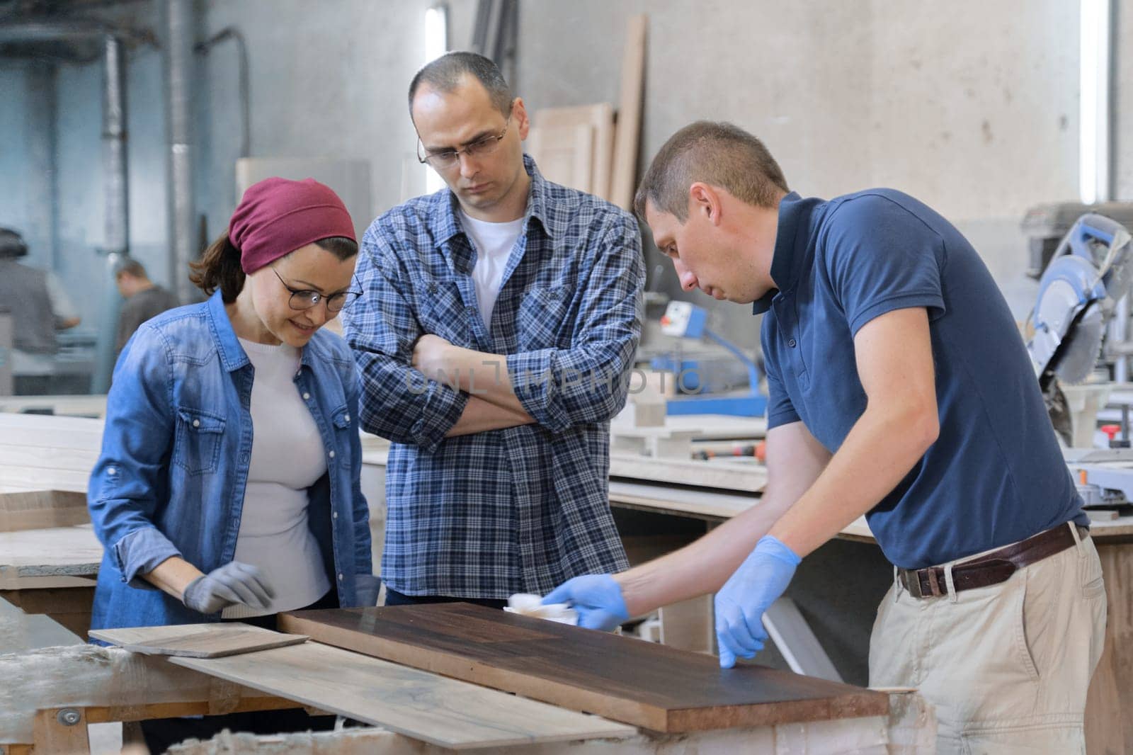 Workers in carpentry woodworking workshop, varnishing wooden plank with oil.