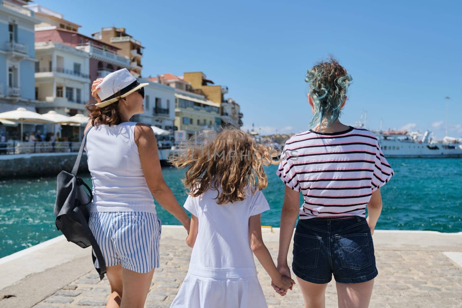 Summer vacation together family mother and daughter children traveling in Mediterranean. Standing with backs on embankment of resort sea town on shore of bay looking at cruise ship