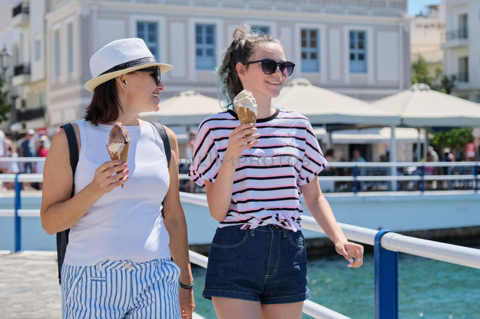 Melting ice cream in hands of smiling walking mother and daughter women on hot sunny summer day on seafront promenade