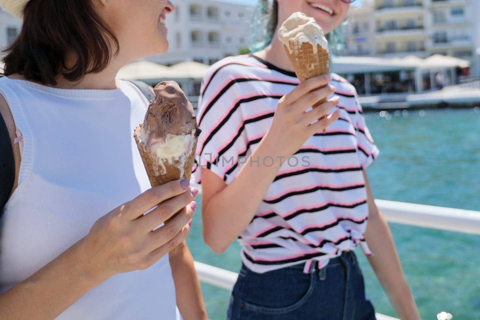 Melting ice cream in hands of smiling walking mother and daughter women on hot sunny summer day on seafront promenade