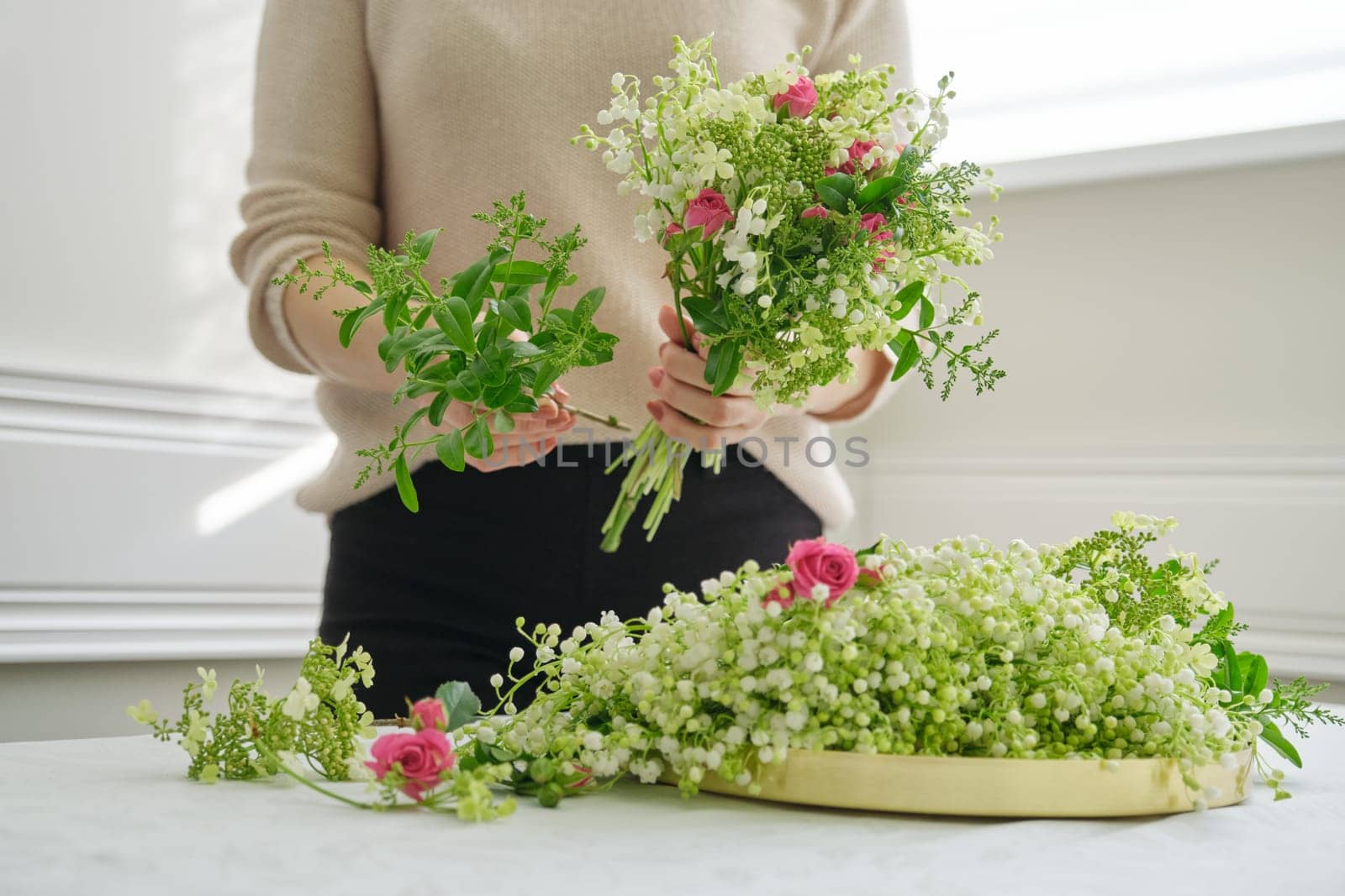 Hands of woman florist making bouquet of flowers pink roses, fresh lily of the valley. by VH-studio