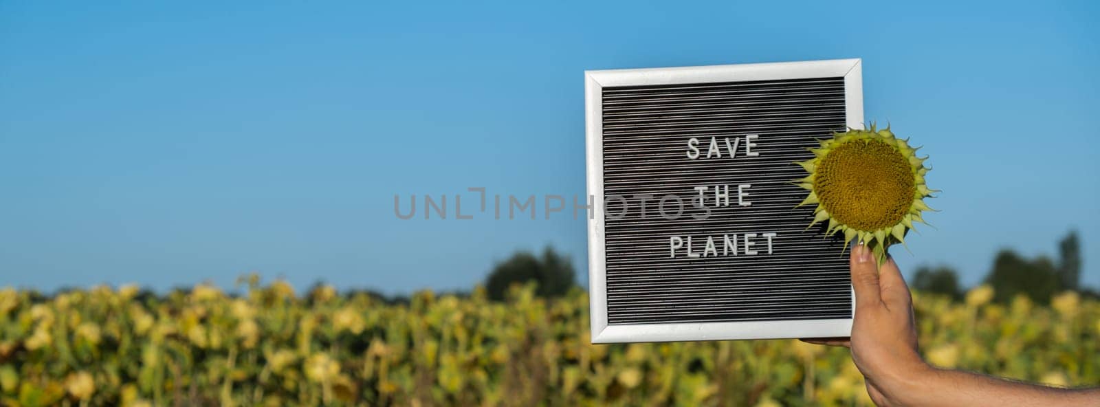 Unrecognizable person with banner message SAVE THE PLANET in sunflower field on sunny day. Sign EARTH day. Concept of ecology and eco activism environmental issues Stop global warming. Go green sustainable