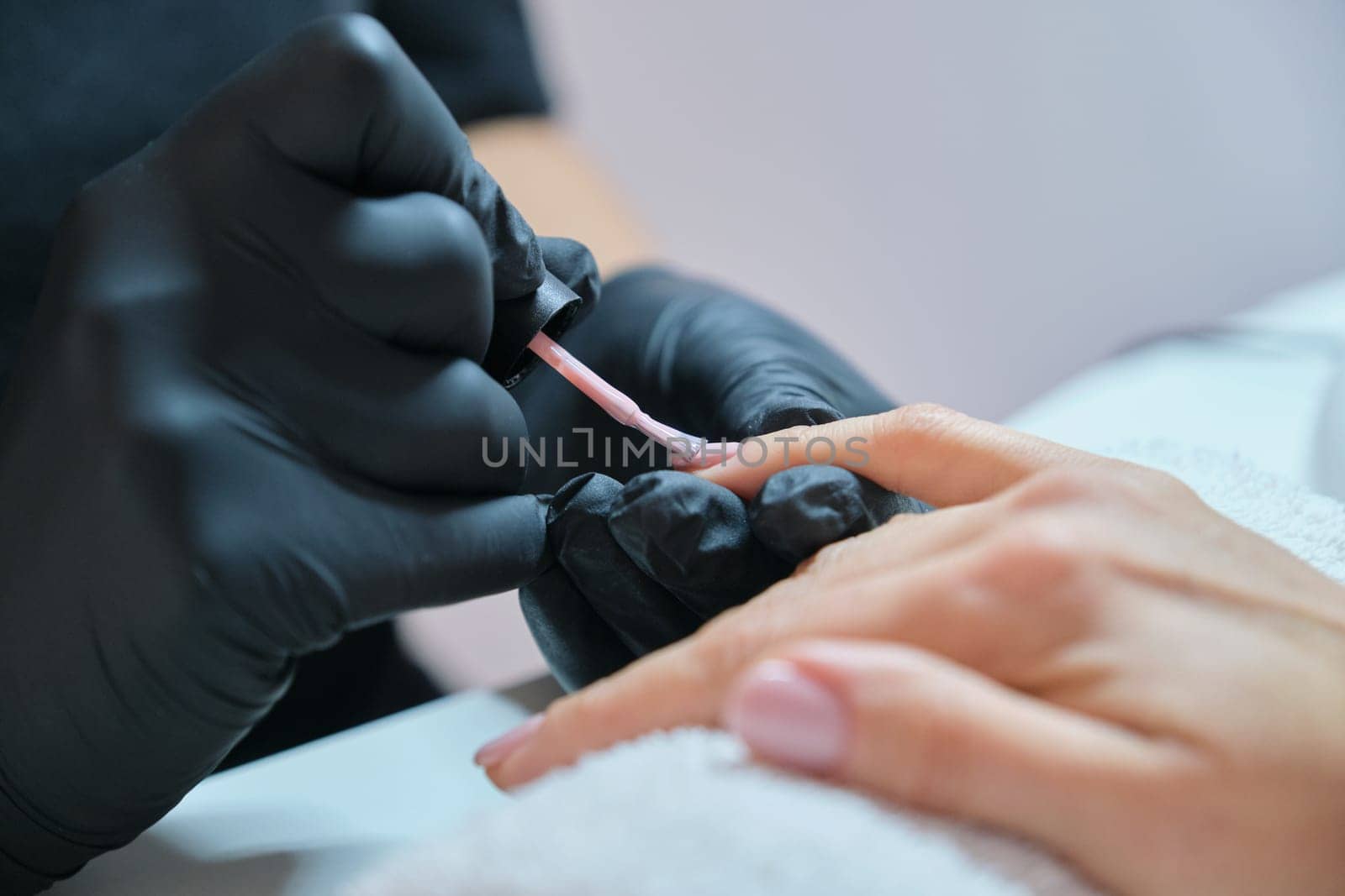 Manicurist varnishes gel nails. Professional hand and nail care in beauty salon.