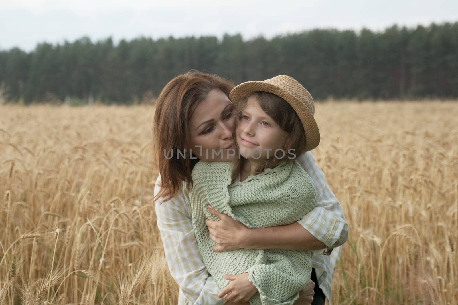 Mother hugging her little daughter, yellow ripe wheat field nature background, sunset golden hour