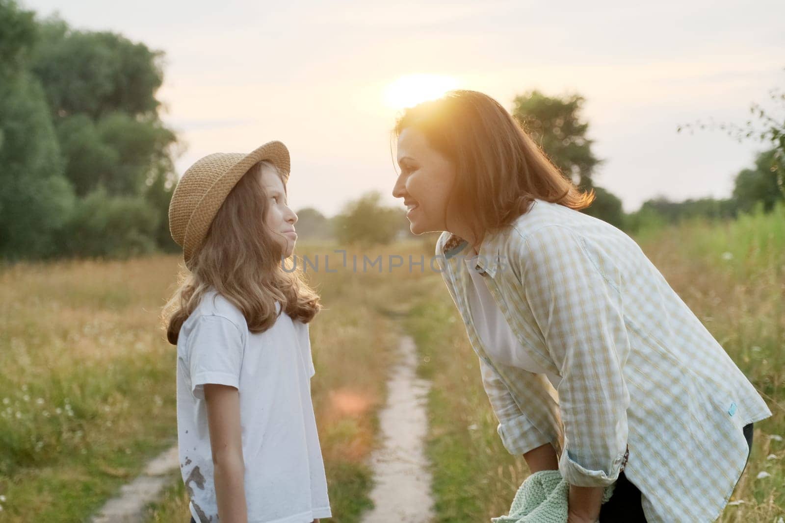 Smiling mother talking with child daughter. Happy loving family, summer nature background golden hour