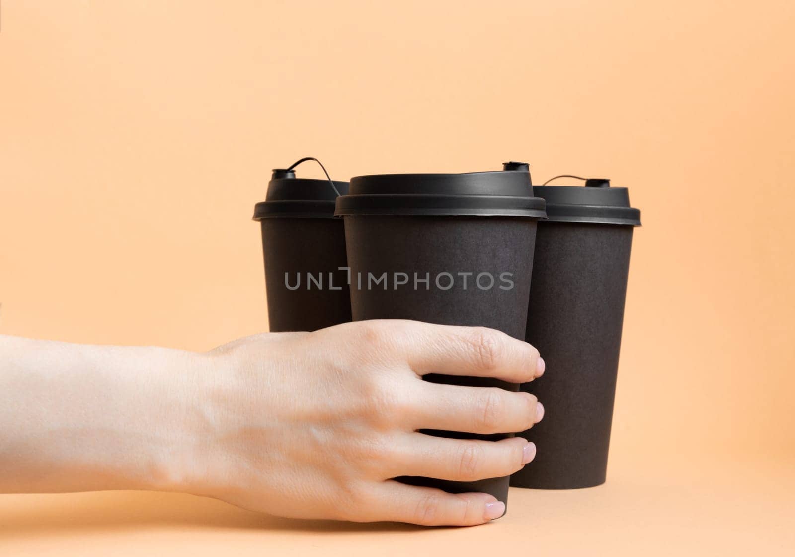 Woman hand holding one black take away coffee cup on neutral pastel background. by Ri6ka
