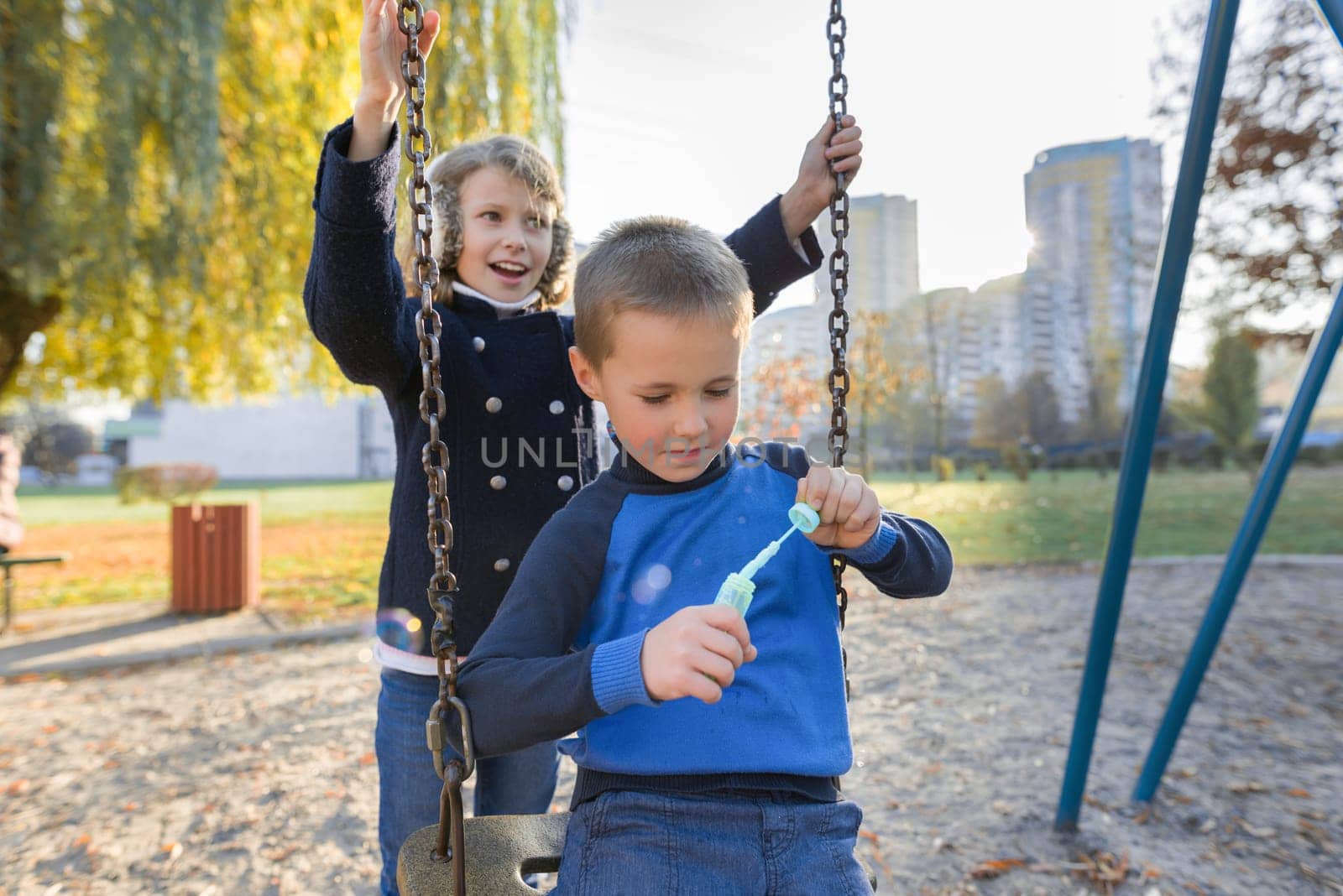 Little boy and girl playing in autumn park, children sitting on swing blow soap bubbles by VH-studio