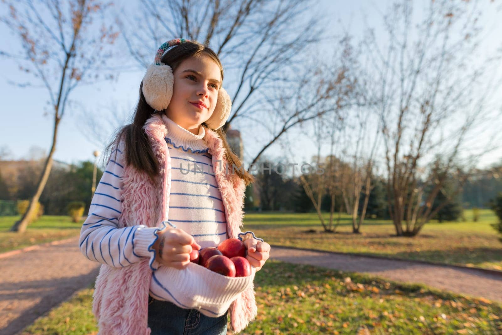 Harvesting, little beautiful girl with apples in autumn park, golden hour copy space