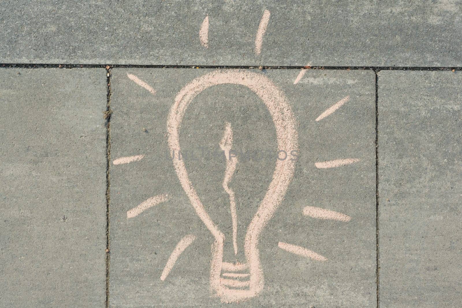 Abstract image drawing of light bulb written on grey sidewalk.