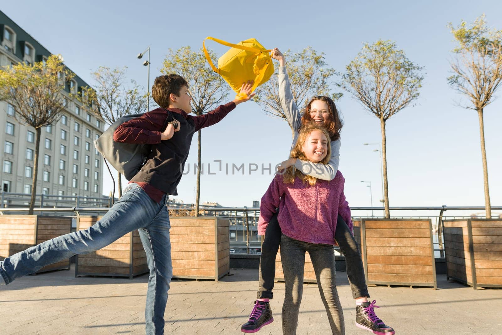 Friends teenagers students with school backpacks, having fun on the way from school. City background, golden hour