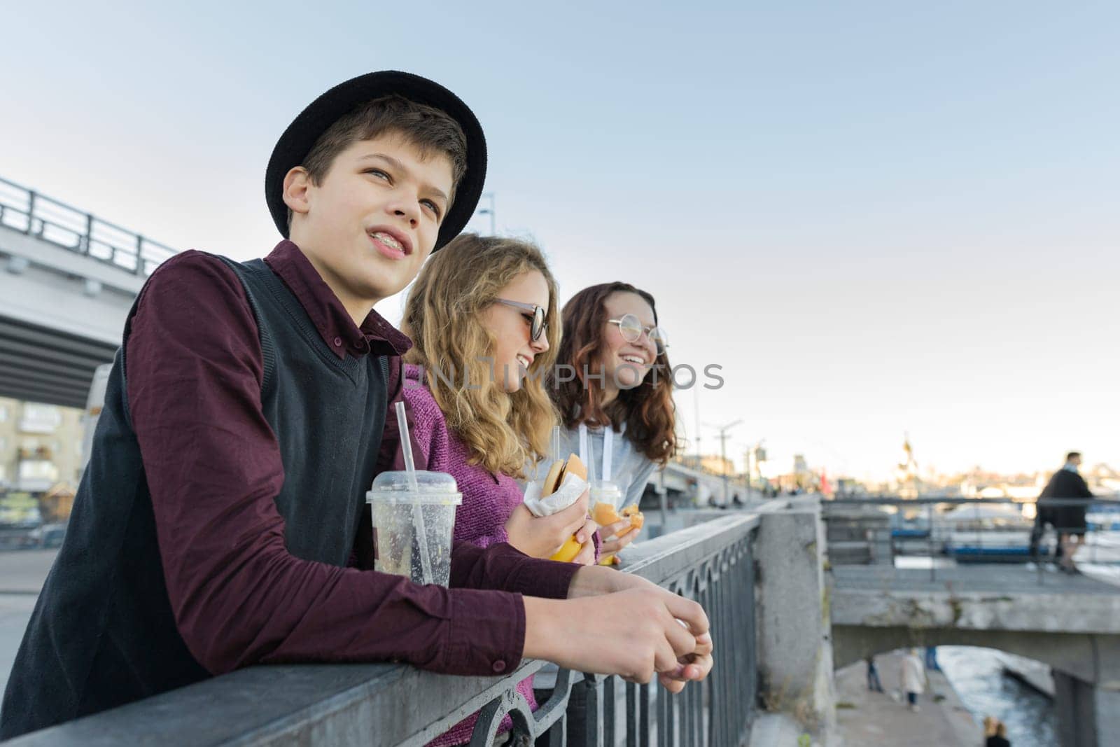 Teenagers boy and two girls with street food talking outdoor.
