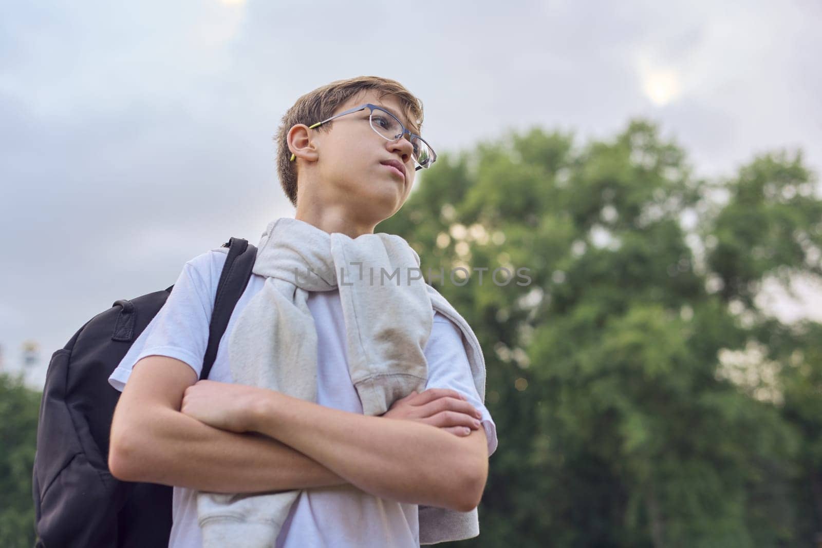 Portrait of teenager schoolboy in glasses with backpack, outdoor boy posing with arms crossed, copy space