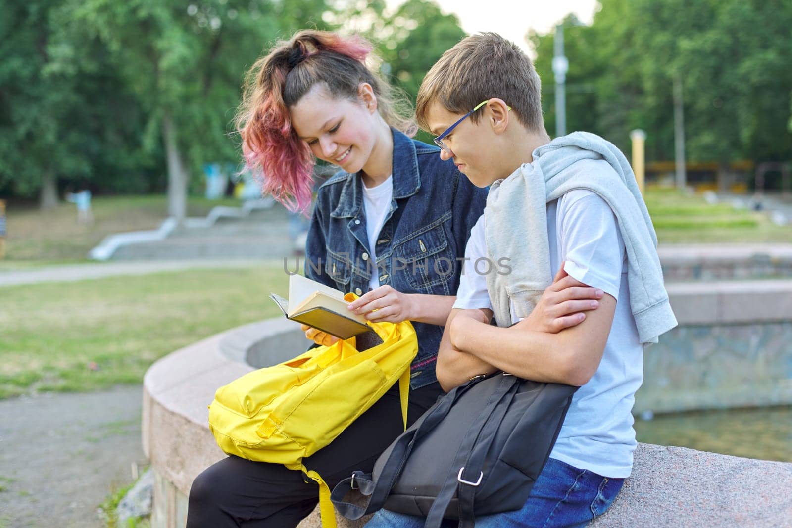 Outdoor portrait of two talking teenagers, students boy and girl with notepad, back to school