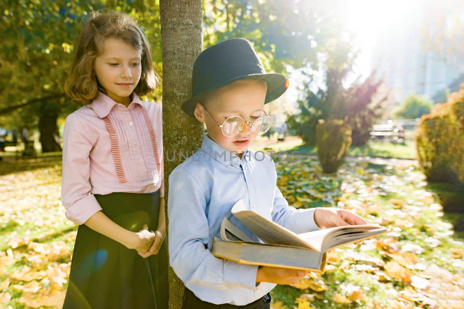 Little boy 6,7 years old with hat, glasses, reading book and girl 7,8 years old by VH-studio