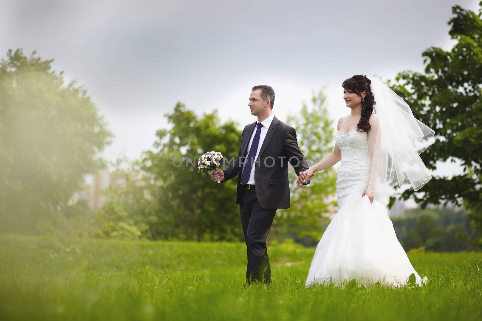 The bride and groom walk on the green grass in the park by Mastak80