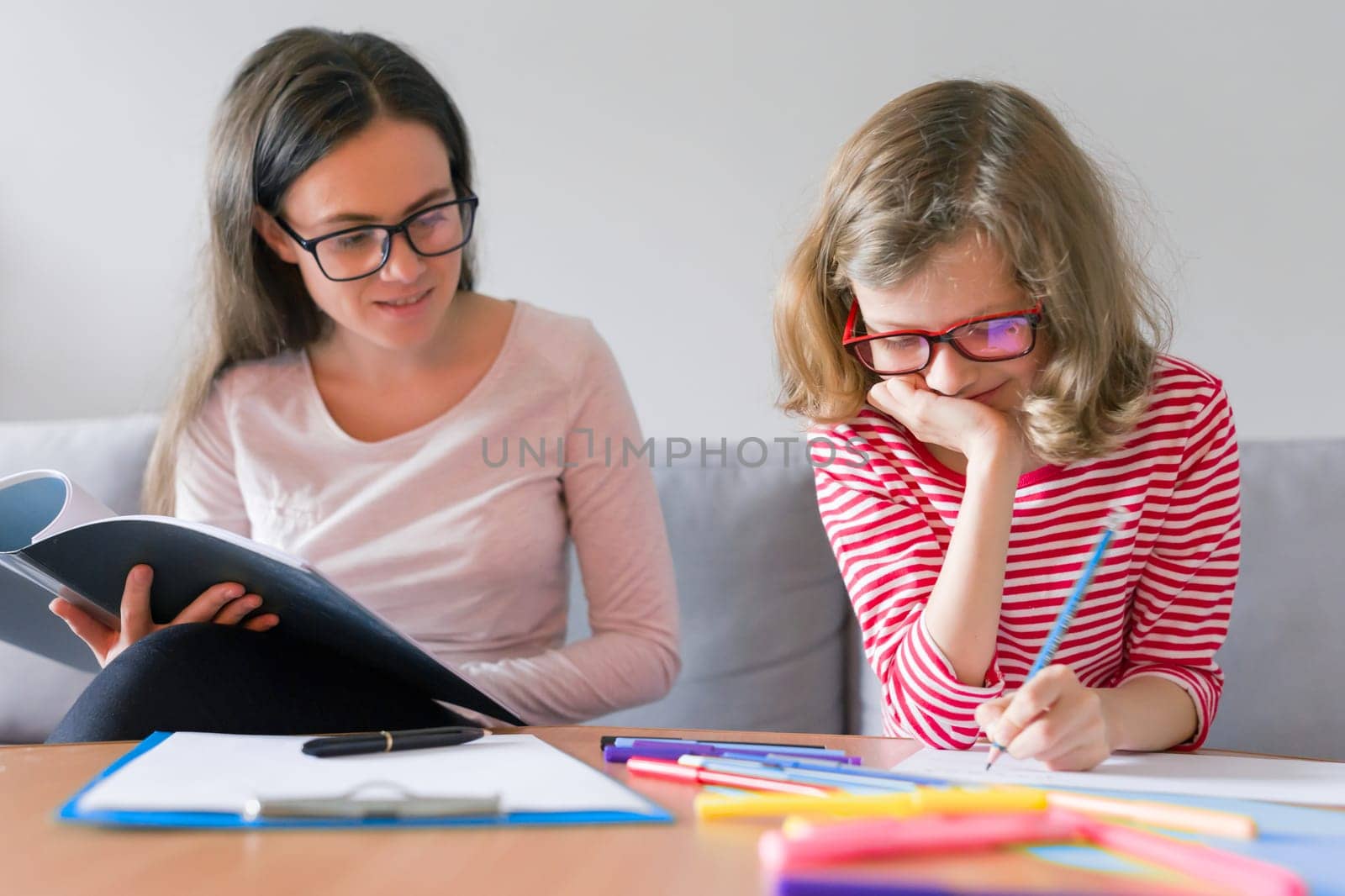 Young woman teacher teaches primary school girl. Individual private education lessons at home
