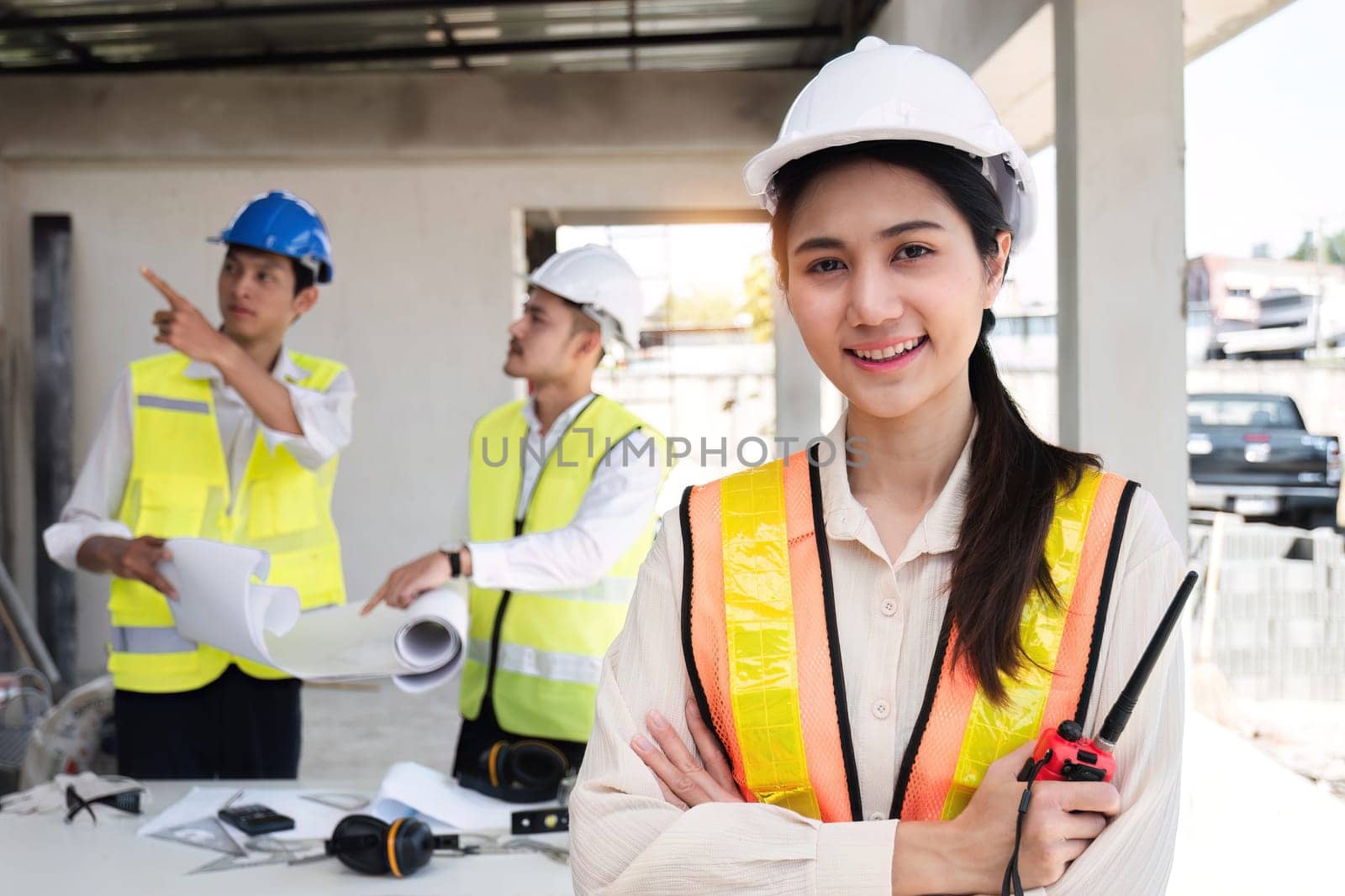 Portrait of a young Asian engineer standing with her arms crossed at a construction site. Portrait of successful young female engineer standing, smiling and looking at camera in engineer's uniform by wichayada